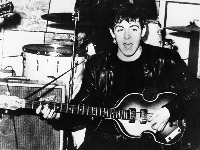 Das schwarz-weiß Foto zeigt den Beatles-Sänger Paul McCartney mit seiner Bass-Gitarre.