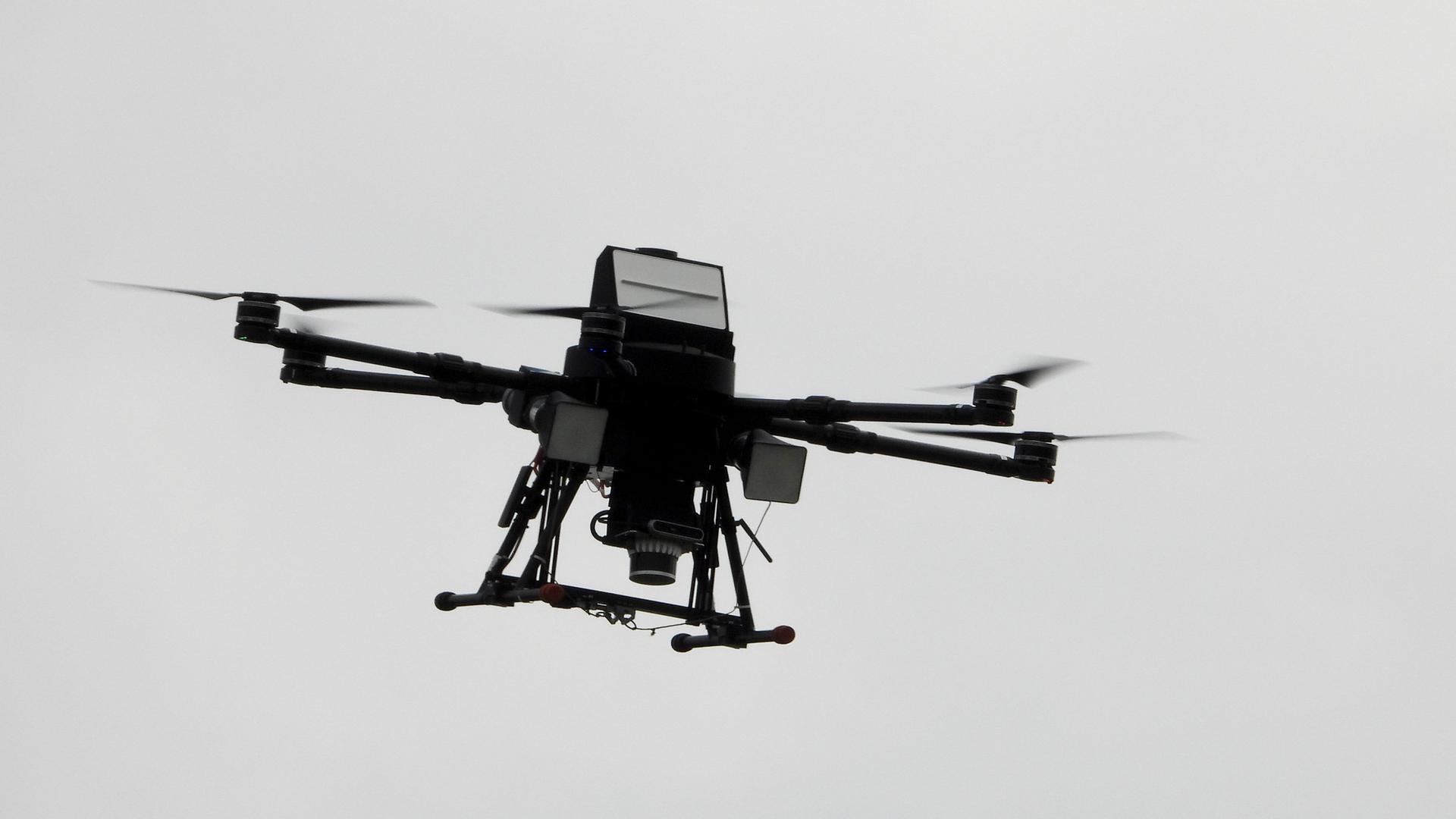 Eine Drohne fliegt im grauen Himmel.