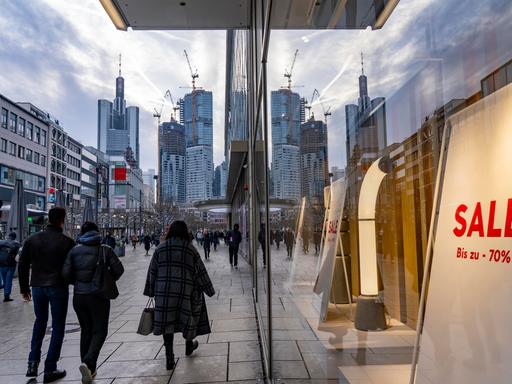 Menschen laufen durch die Einkaufsstraße Zeil in Frankfurt am Main, am Horizont ist die Skyline zu sehen.
