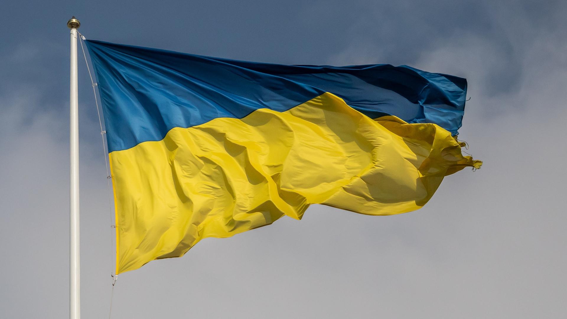 Eine ukrainische Fahne flattert in Kiew im Wind, im Hintergrund blauer Himmel