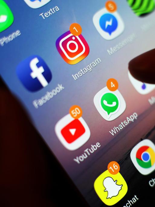 Ein Finger zeigt auf Apps wie Facebook, Instagram, Youtube und WhatsApp auf einem Smartphone-Bildschirm.