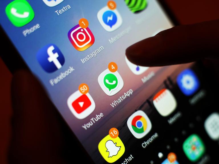 Ein Finger zeigt auf Apps wie Facebook, Instagram, Youtube und WhatsApp auf einem Smartphone-Bildschirm.