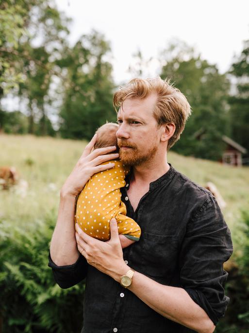 Ein nachdenklich schauender Vater mit einem kleinen Baby im Arm.