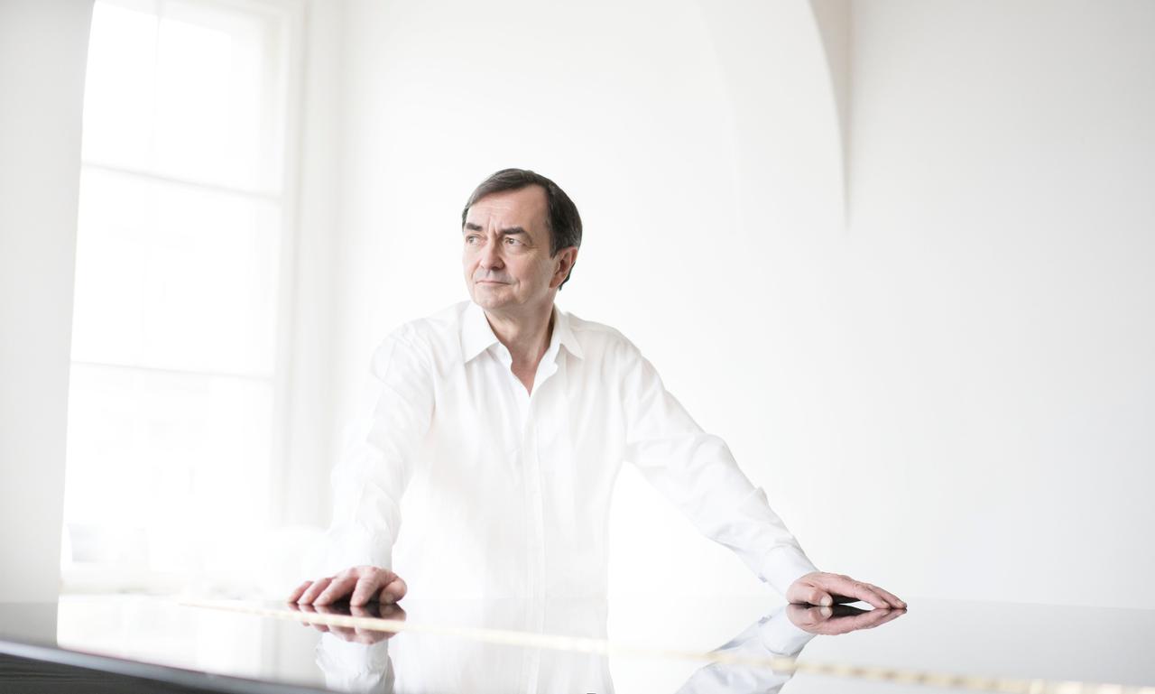 Der ganz in weiß gekleidete Pianist steht in einem weißen Raum mit großem Fenster und hat beide Arme auf einen geschlossenen Flügel gestützt. Der ganz in weiß gekleidete Pianist steht in einem weißen Raum mit großem Fenster und hat beide Arme auf einen geschlossenen Flügel gestützt.