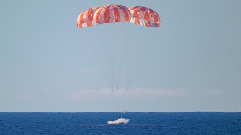Der Moment der Wasserung im Pazifik. Die Orion-Kapsel hängt an drei rot-weißen Fallschirmen.