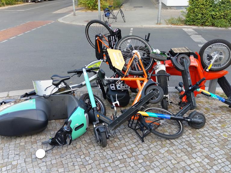 Elekto-Roller, E-Tretroller sowie Leihräder liegen von Unbekannten aufeinandergetürmt an einer Kreuzung in Berlin-Schöneberg auf dem Bürgersteig. 