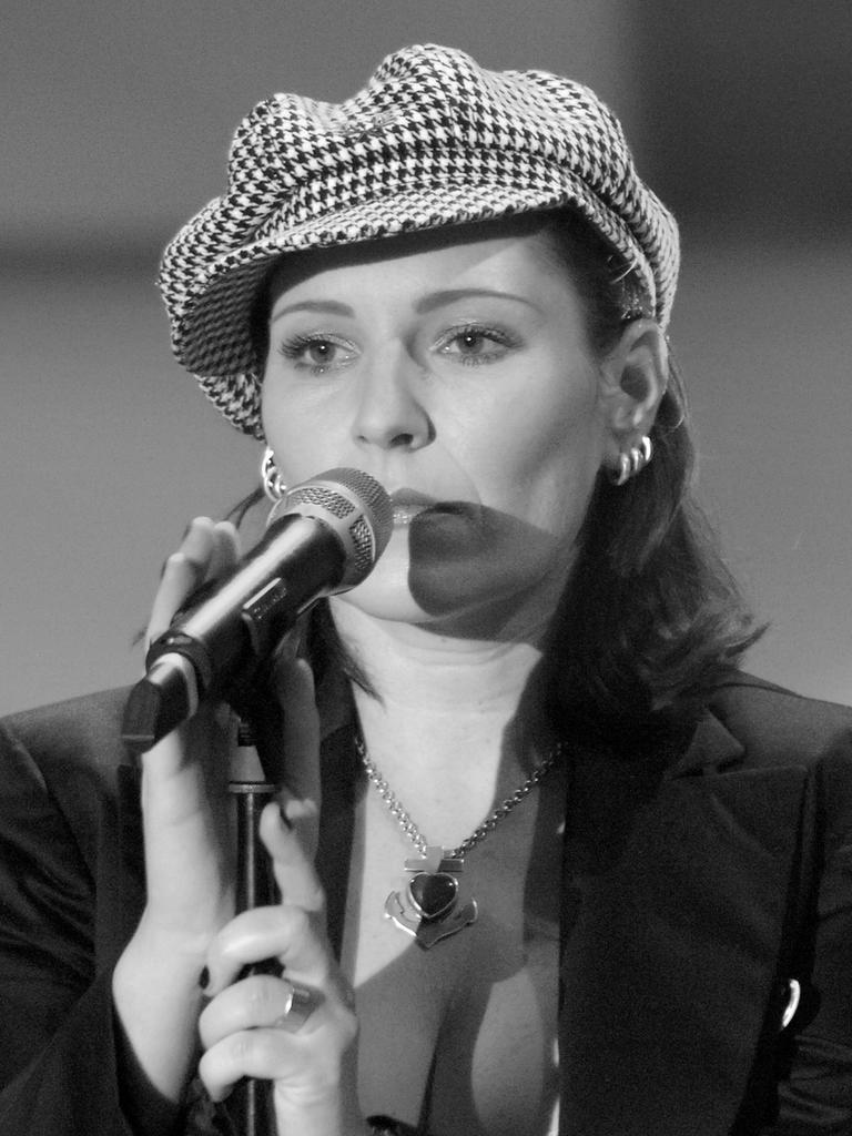 Anna R., Sängerin der Gruppe Rosenstolz, bei einem Auftritt. Sie trägt eine Mütze und singt in ein Mikrophon. 
