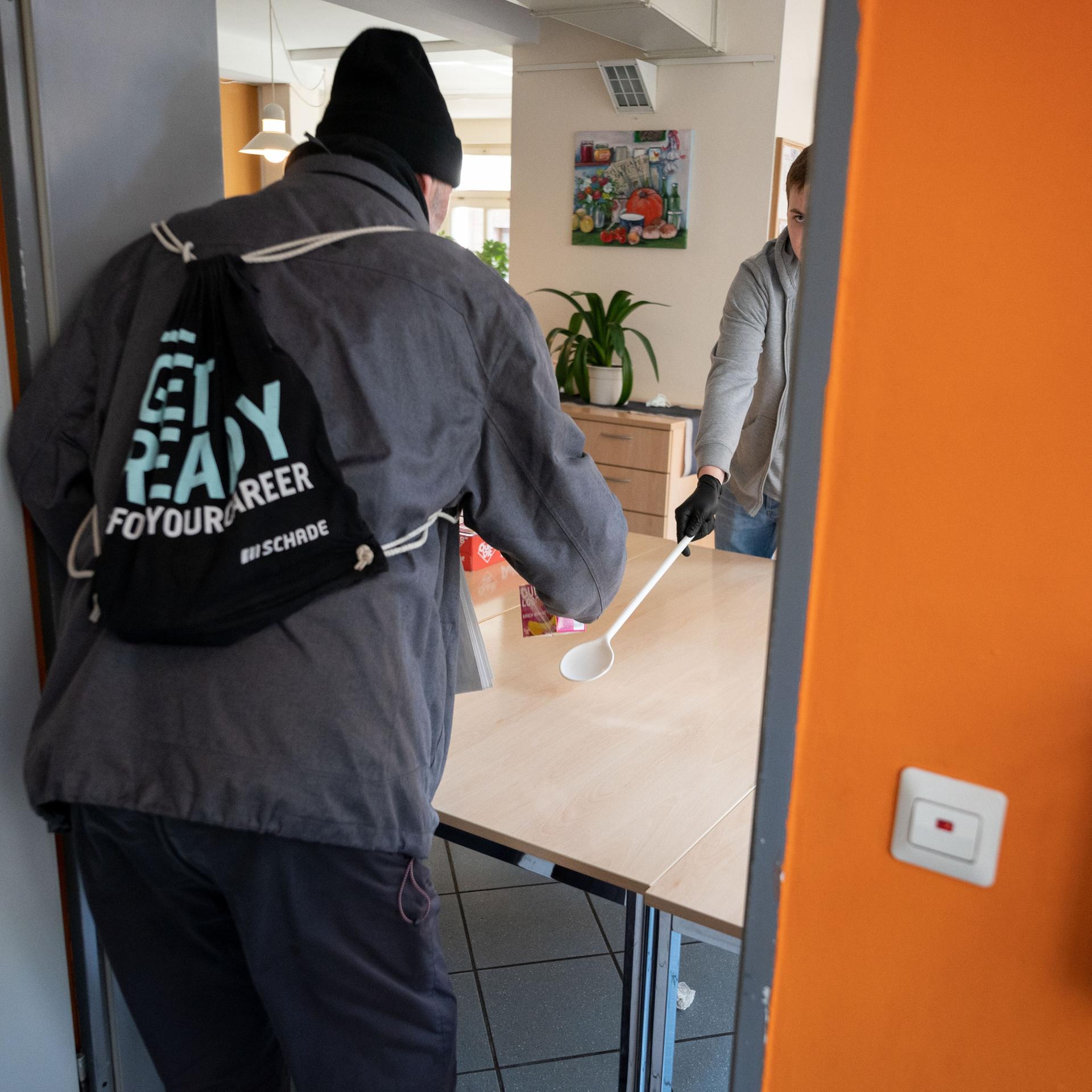 Ein junger Mann arbeitet in der Obdachlosentagesstätte Olga 46. Es ist sein Freiwilliges Soziales Jahr. Er reicht einem Mann ein Getränk. Das Foto ist von 2020.