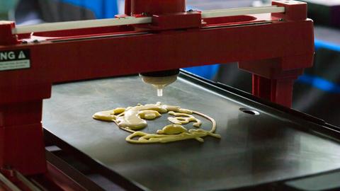 Ein 3D-Drucker druckt flüssigen Teig auf ein Blech.