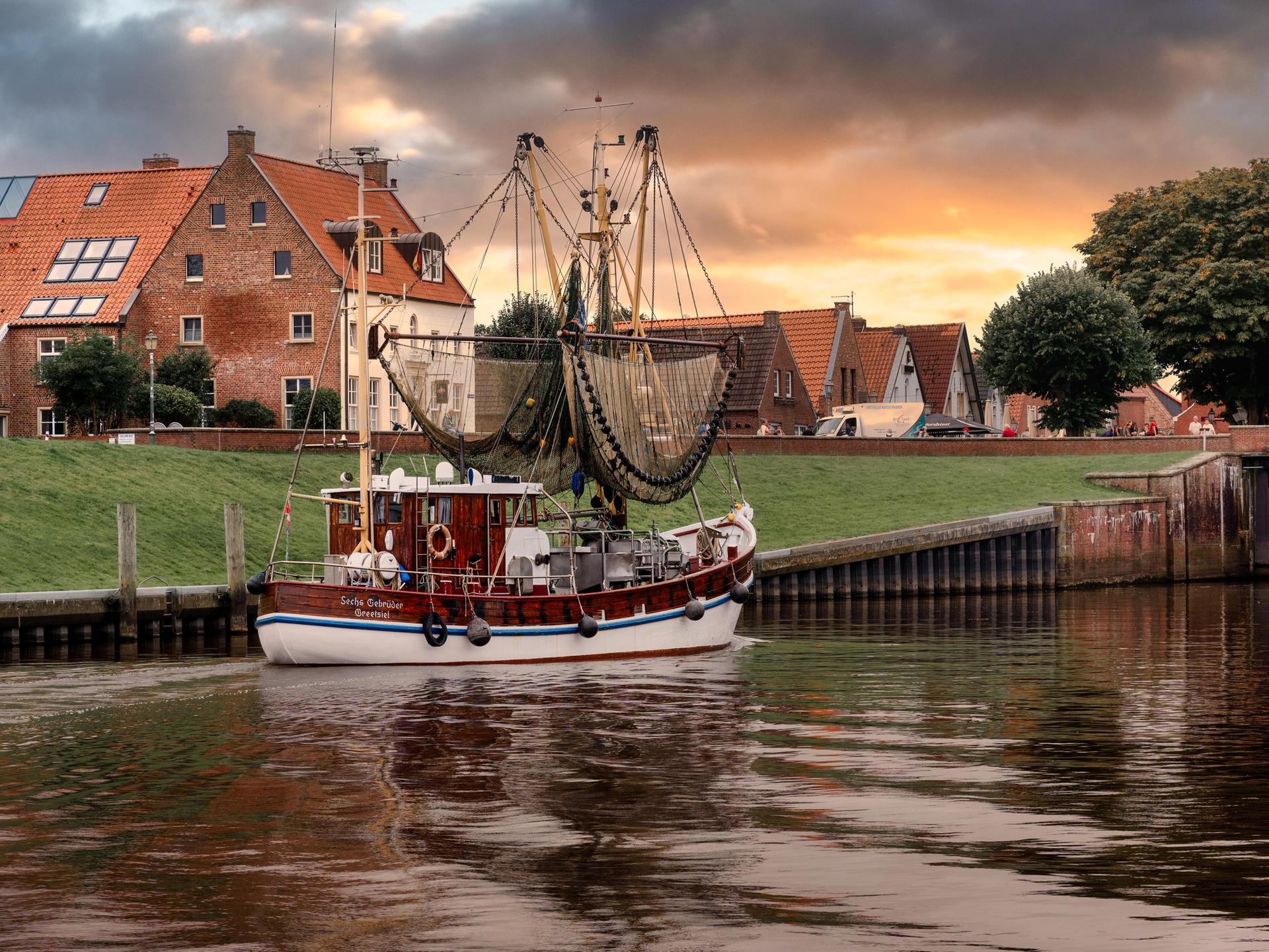 Der Nordseehafen Greetsiel mit traditionellen Backsteinbauten und einem kleinen Fischerboot im Vordergrund in der Abendsonne 