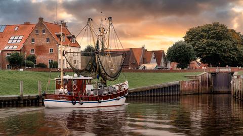 Der Nordseehafen Greetsiel mit traditionellen Backsteinbauten und einem kleinen Fischerboot im Vordergrund in der Abendsonne 