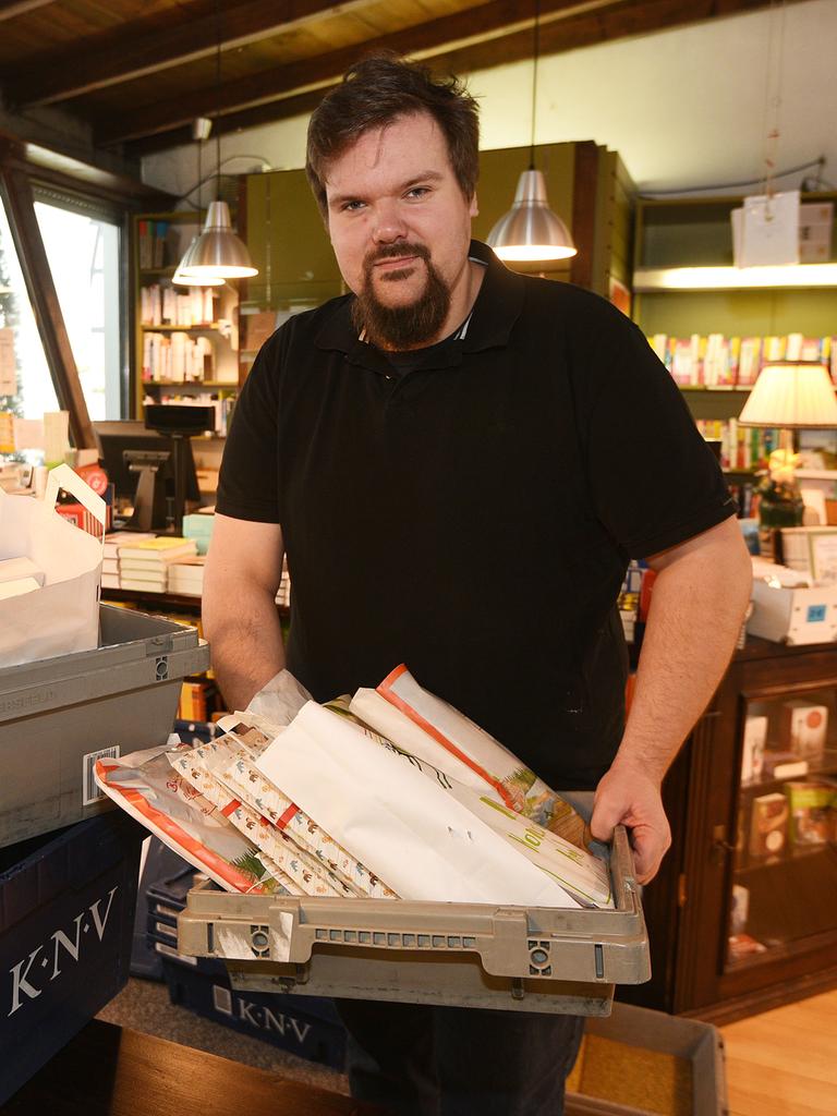 Dennis Hasemann steht in einer Buchhandlung, vor ihm eine Kiste mit Büchern, im Hintergrund Bücherregale.