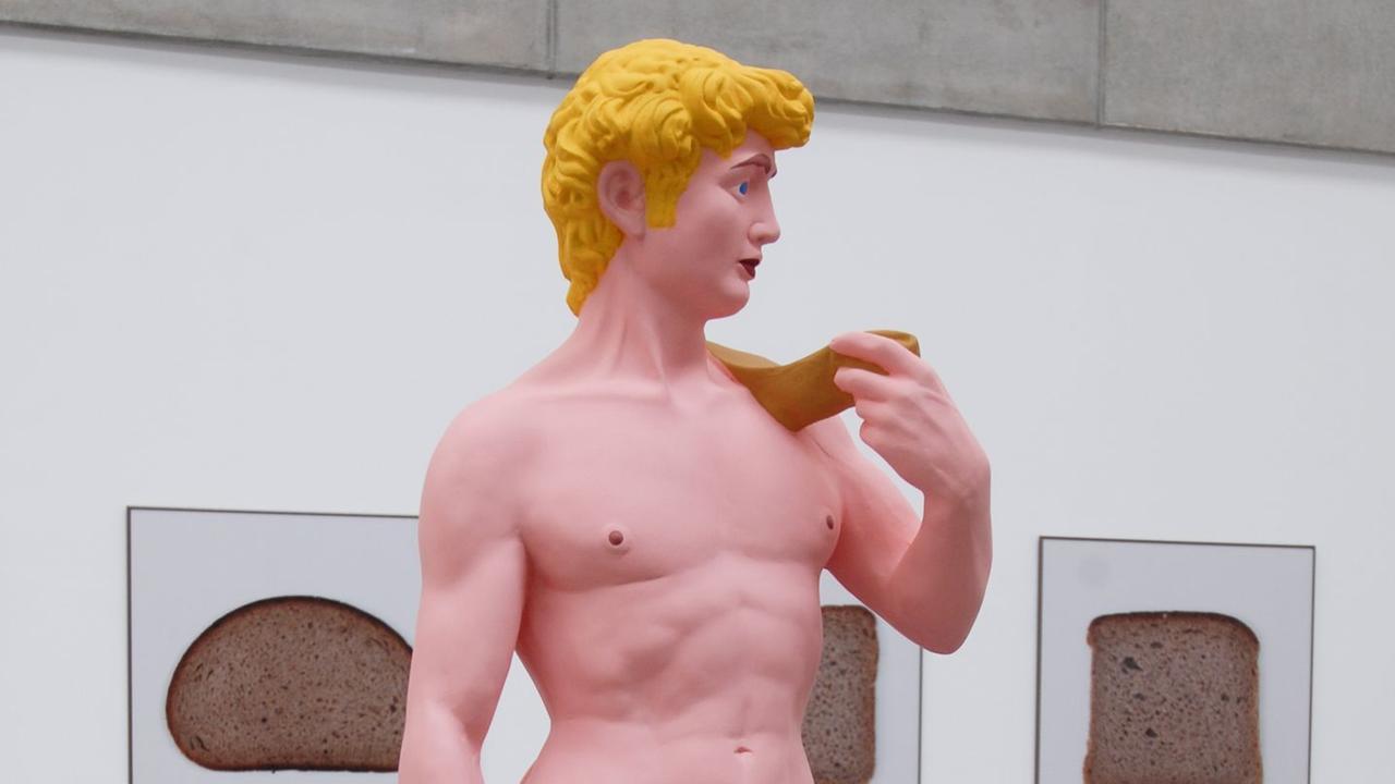 Die Skulptur eines nackten Mannes erinnert an den David von Michelangelo. Der Körper ist rosafarben, die Haare sind gelb.
