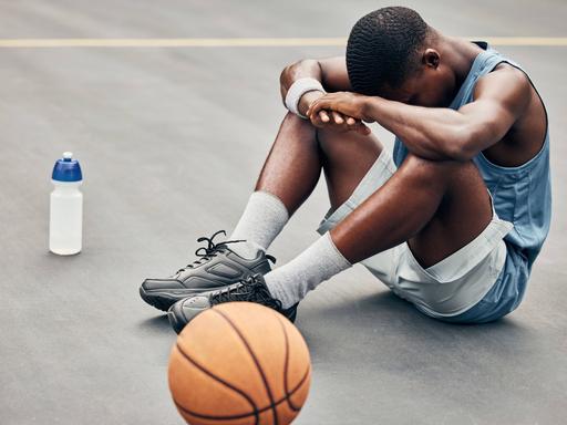Ein Basketballer sitzt am Boden, er vergräbt den Kopf zwischen den Knien.