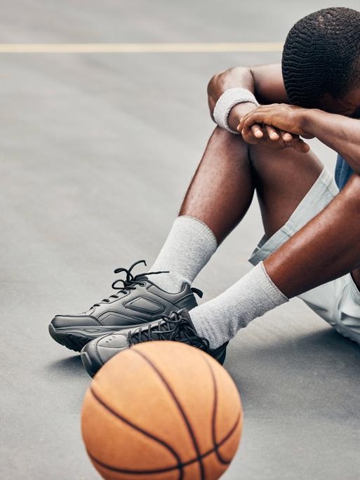 Ein Basketballer sitzt am Boden, er vergräbt den Kopf zwischen den Knien.