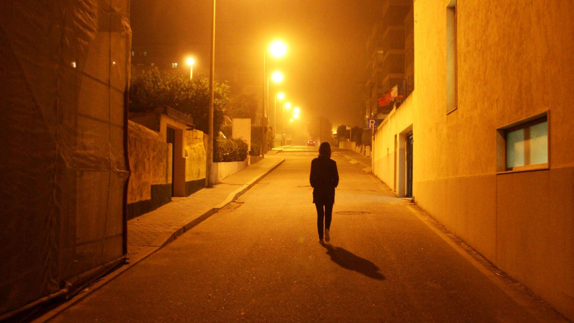 Eine Frau läuft bei Nacht auf einer Straße durch ein menschenleeres Wohngebiet.