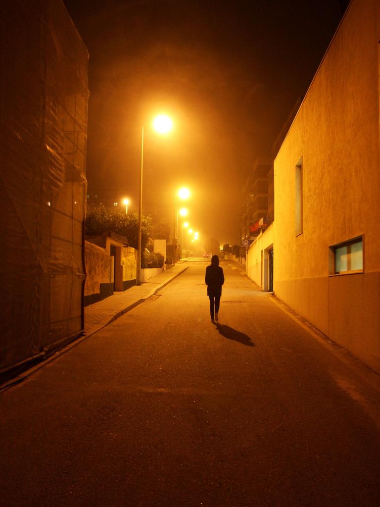 Eine Frau läuft bei Nacht auf einer Straße durch ein menschenleeres Wohngebiet.