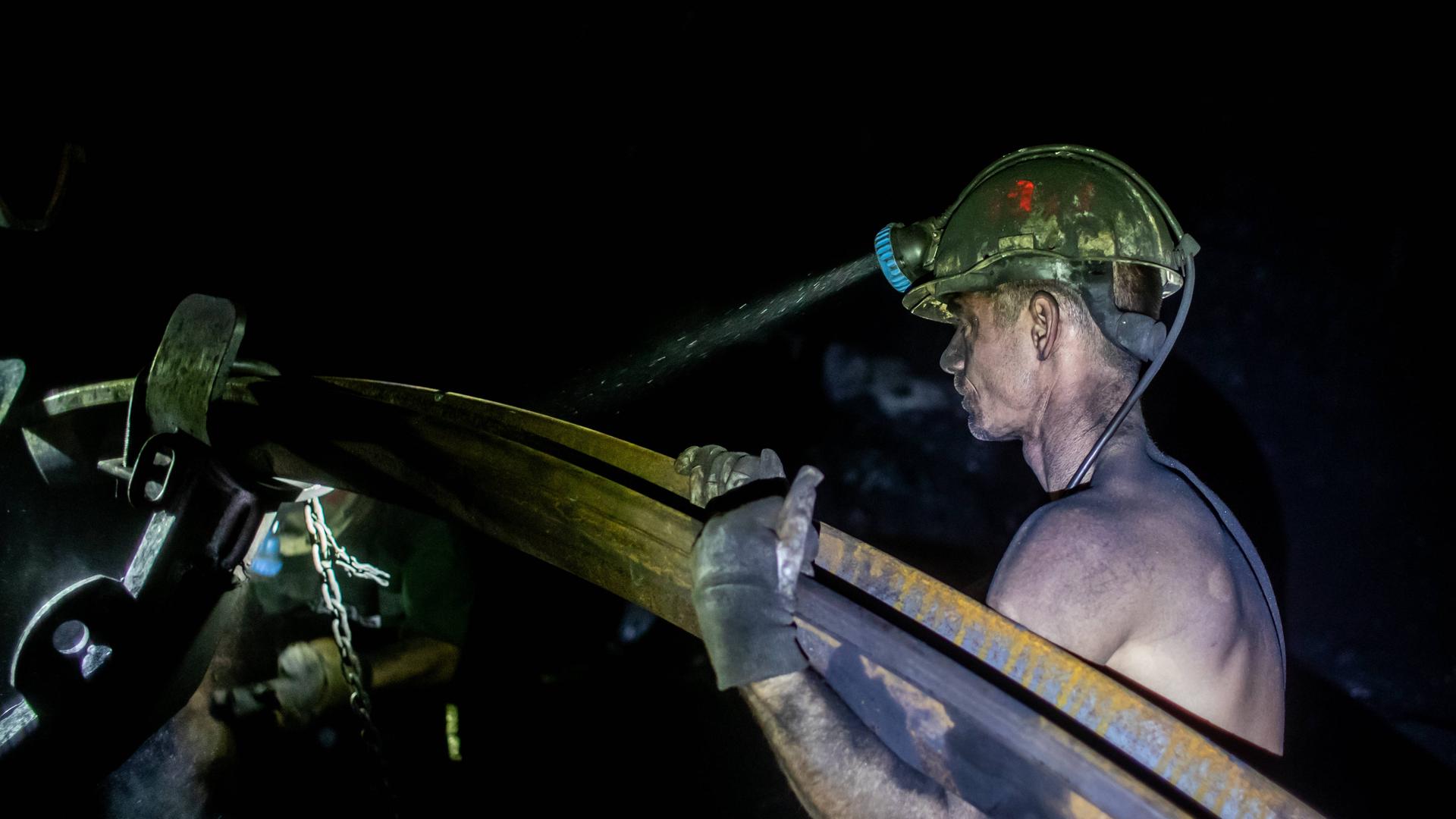 Ein mit Kohlenstaub bedeckter Bergmann trägt mit freiem Oberkörper ein schweres Metallrohr. Von seinem gelben Helm strahlt die Grubenlampe in die Dunkelheit der Kohlenmine. Stonava near Karvinâa, Czech Republicâ, January 22, 2025. Ein mit Kohlenstaub bedeckter Bergmann trägt mit freiem Oberkörper ein schweres Metallrohr. Von seinem gelben Helm strahlt die Grubenlampe in die Dunkelheit der Kohlenmine. Stonava near Karvinâa, Czech Republicâ, January 22, 2025.