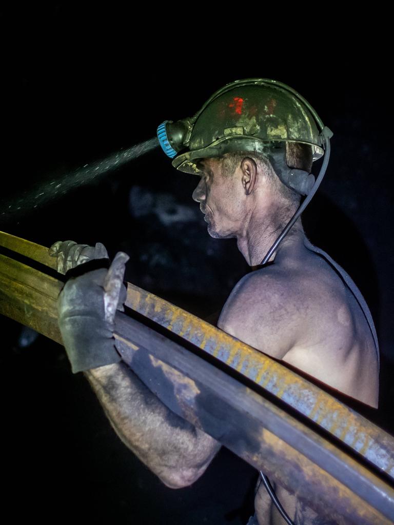 Ein mit Kohlenstaub bedeckter Bergmann trägt mit freiem Oberkörper ein schweres Metallrohr. Von seinem gelben Helm strahlt die Grubenlampe in die Dunkelheit der Kohlenmine. Stonava near Karvinâa, Czech Republicâ, January 22, 2025. 