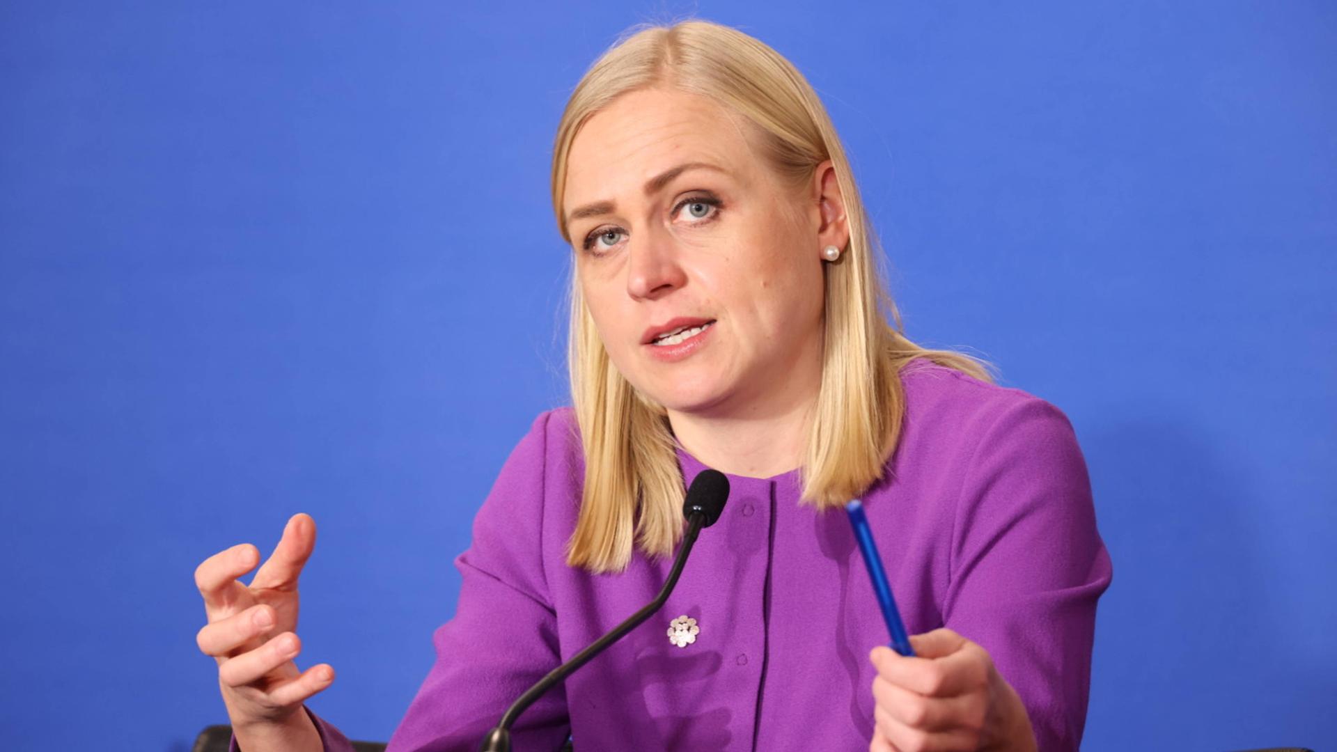 Elina Valtonen sitzt in Wien auf einem Podium vor einer blauen Wand an einem Mikrofon und gestikuliert.