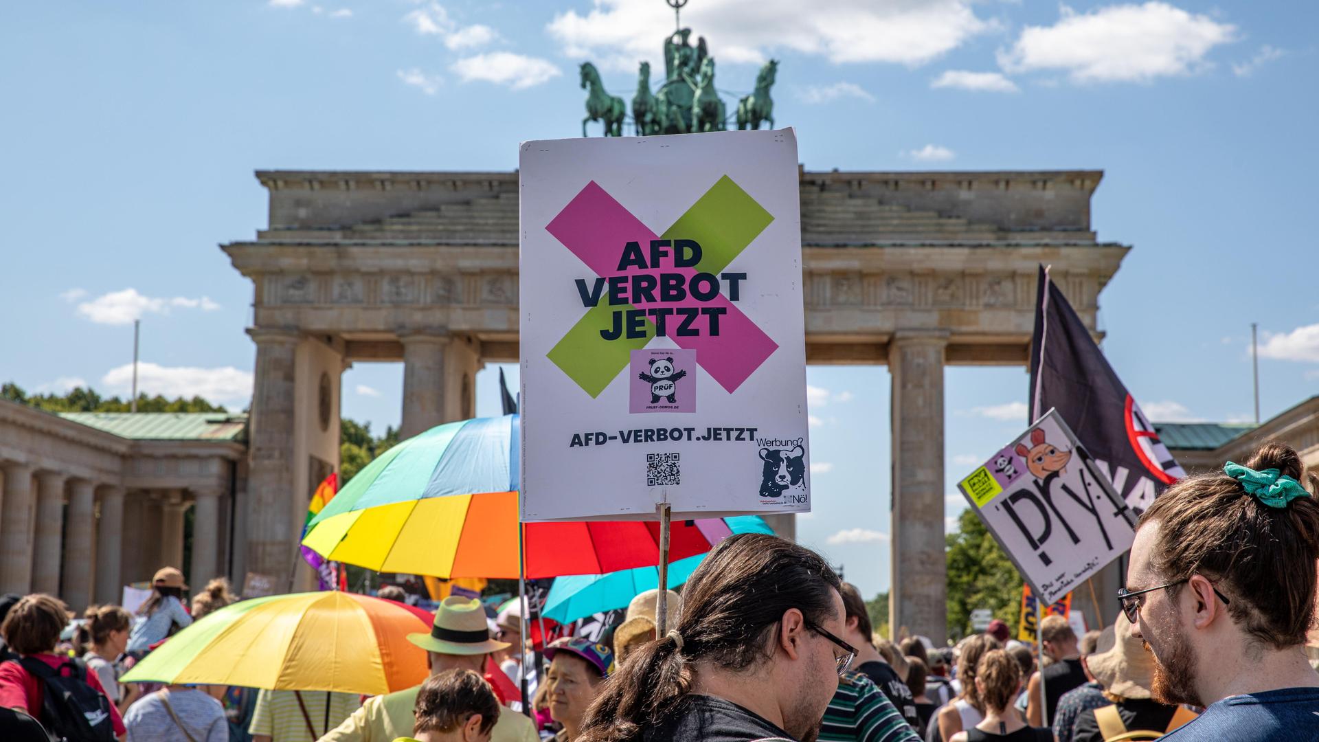 Das Bild zeigt ein Protestschild. Darauf steht "AFD VERBOT JETZT". Im Hintergrund ist das Brandenburger Tor in Berlin zu erkenen. Das Bild zeigt ein Protestschild. Darauf steht "AFD VERBOT JETZT". Im Hintergrund ist das Brandenburger Tor in Berlin zu erkenen.