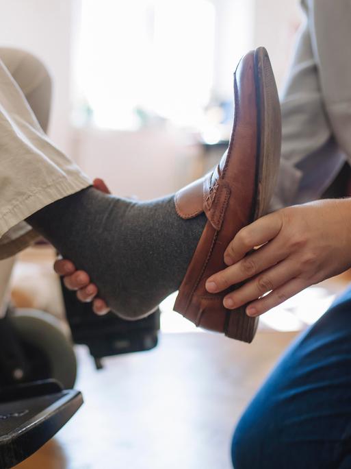 Einem Mann im Rollstuhl wird der Schuh ausgezogen.