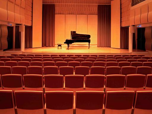 Ein leerer Konzertsaal. Auf der Bühne steht ein Flügel mit Hocker davor.