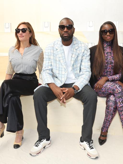 Die Models Audrey Diwan, Abd al Malik und Karidja Toure sitzen bei der Chanel Fashion Show nebeneinander und präsentieren ihre Kleidung