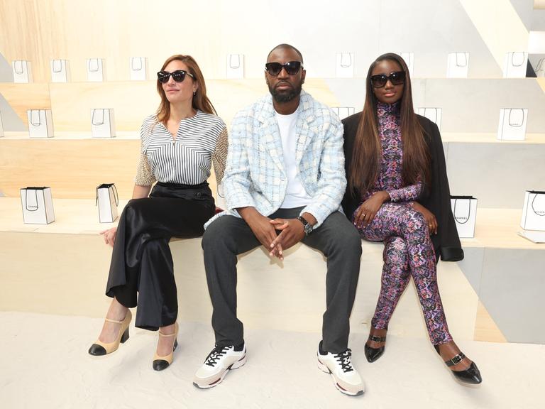 Die Models Audrey Diwan, Abd al Malik und Karidja Toure sitzen bei der Chanel Fashion Show nebeneinander und präsentieren ihre Kleidung