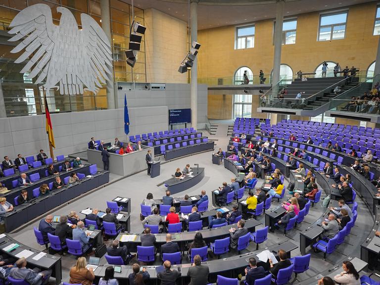 Der Plenarsaal des Bundestags: An der Wand hängt der Bundesadler, Abgeordnete sitzen auf den blauen Bundestagsstühlen.