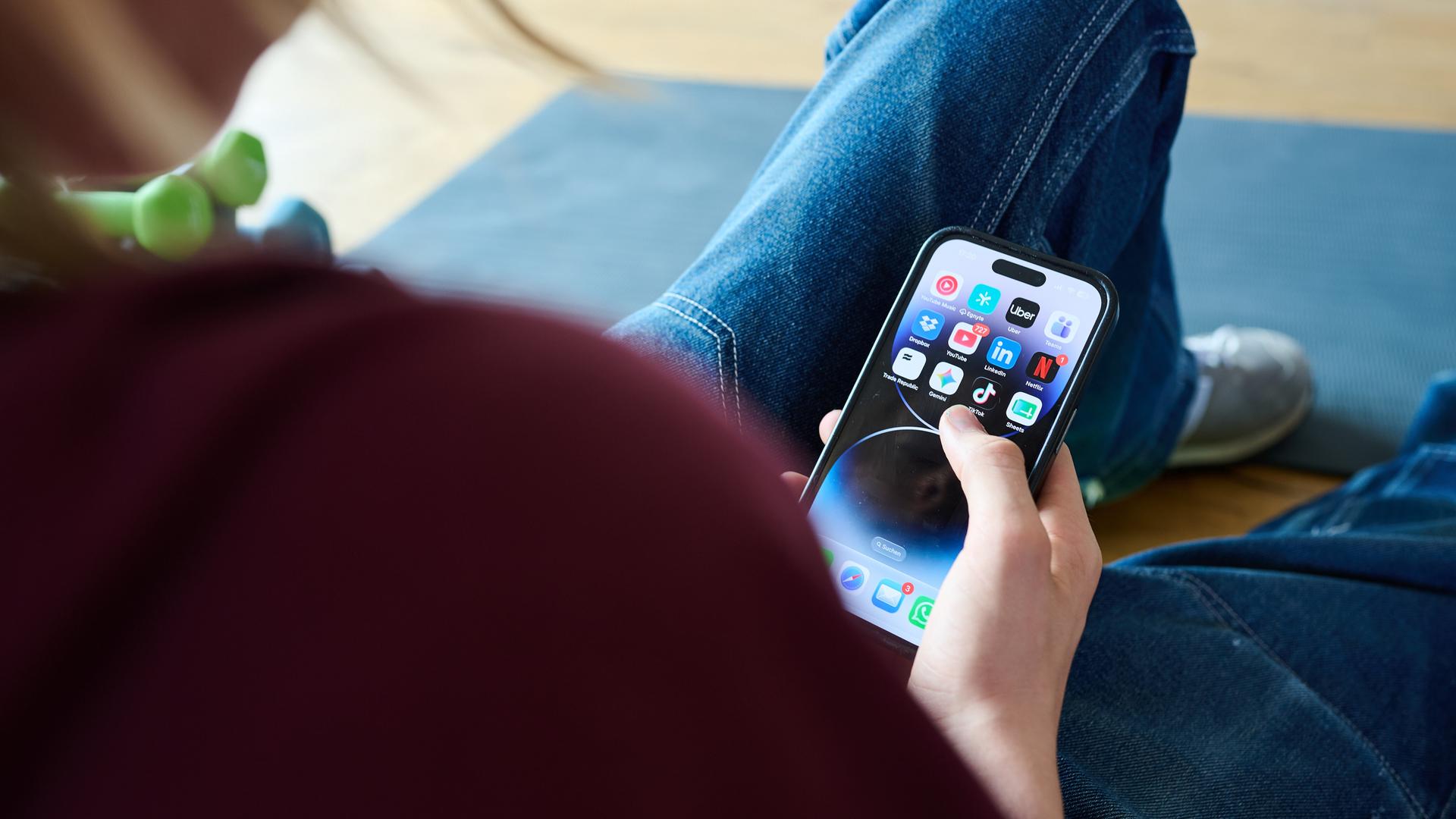 Ein Teenager sitzt am Boden und guckt auf ein Handy.
