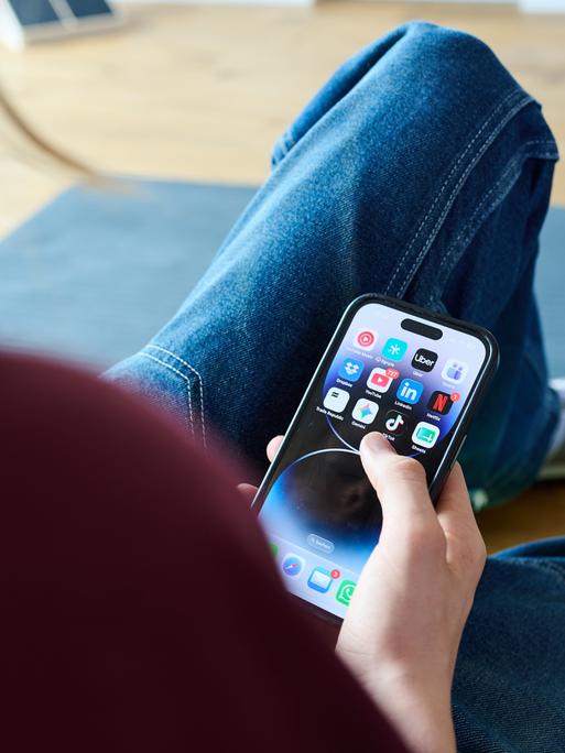 Ein Teenager sitzt am Boden und guckt auf ein Handy. Ein Teenager sitzt am Boden und guckt auf ein Handy.
