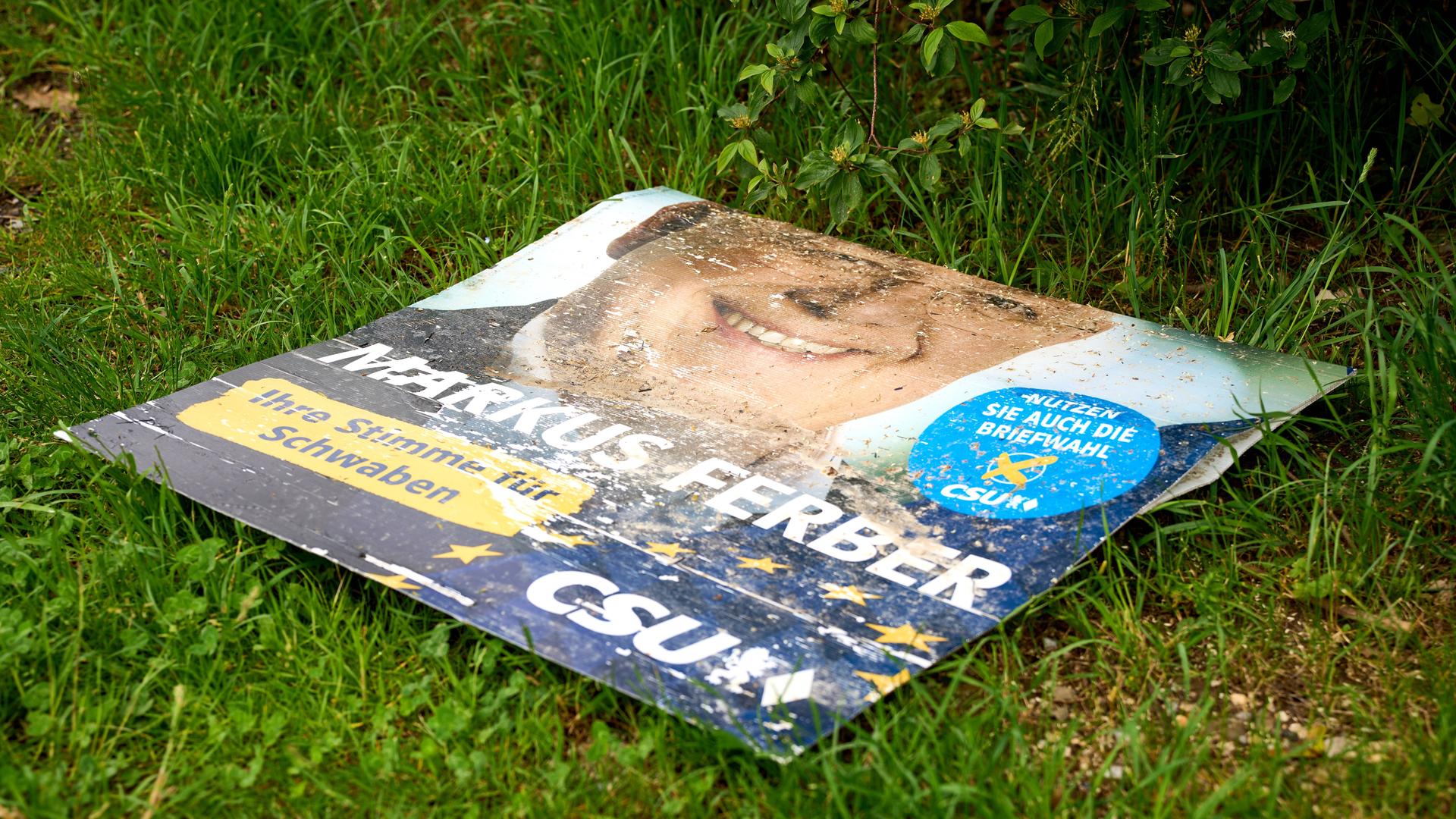 Ein Wahlplakat des CSU-Kandidaten Markus Ferber liegt zerstört auf einer Wiese.