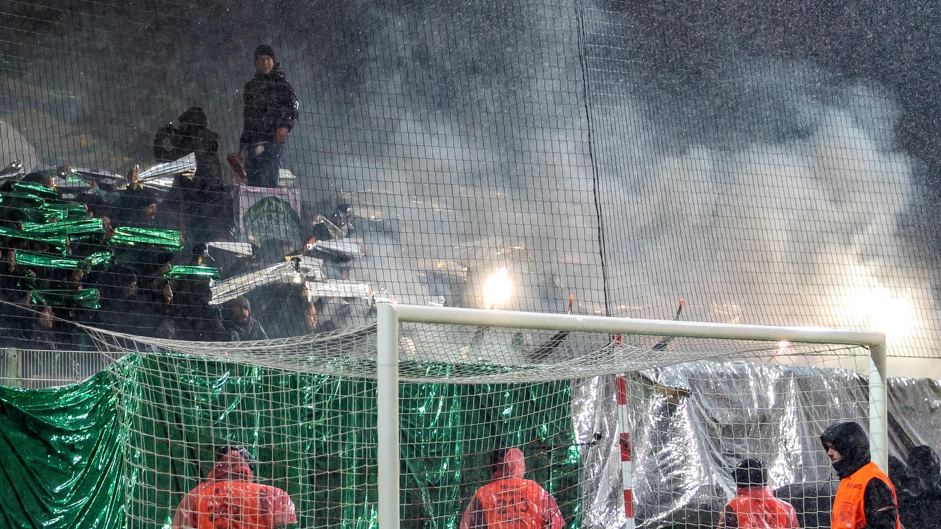 Rauch steigt über den Sitzreihen im Stadion auf, mehrere Menschen in Warnwesten stehen davor.