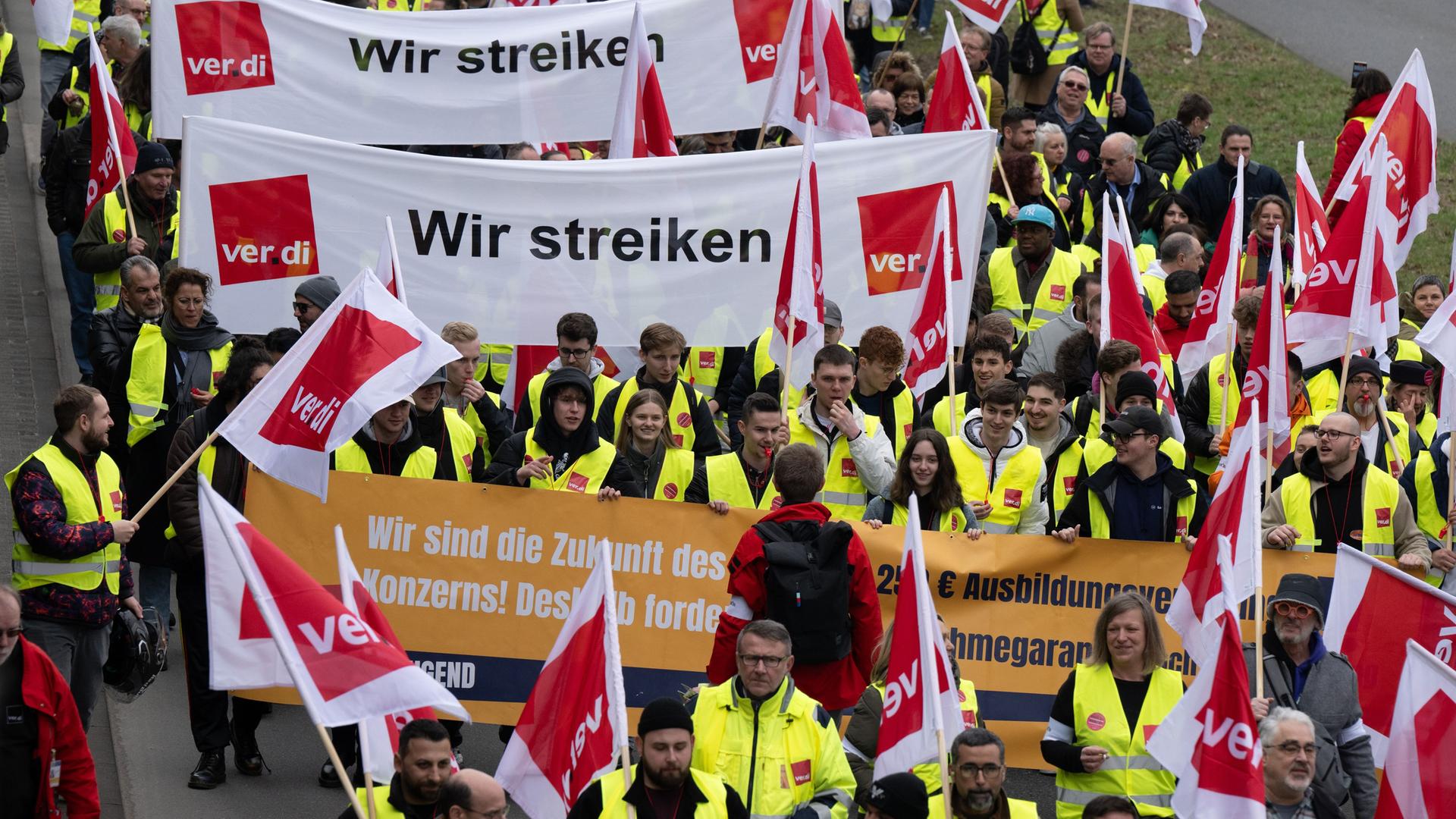 Blick von vorn auf einen Demonstrationszug: Die Teilnehmer tragen gelbe Warnwesten; einige von ihnen tragen Transparente und Fahnen.