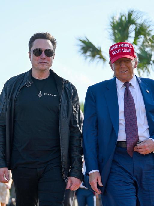 Donald Trump und Elon Musk laufen unter Palmen nebeneinander her. 