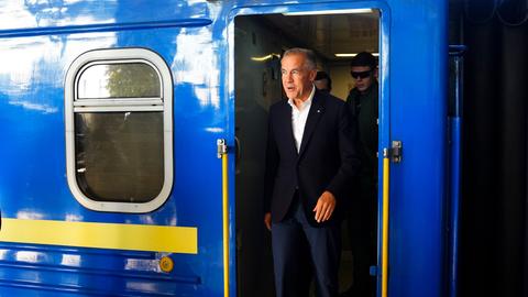 Ein Mann steht in der Türöffnung eines Zugs. Der Zug ist blau-geb lackiert.