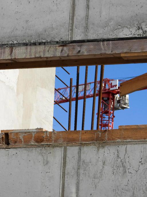 Blick durch eine Fensterlücke im Rohbau eines Wohnhauses mit Krahn im Hintergrund