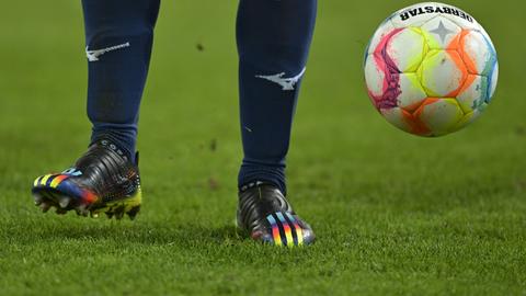 Szene aus dem Fußball-Bundesligaspiel FC Augsburg - VfL Bochum mit Regenbogenfarben auf dem Schuh eines Bochumer Spieler und auf dem Spielball

