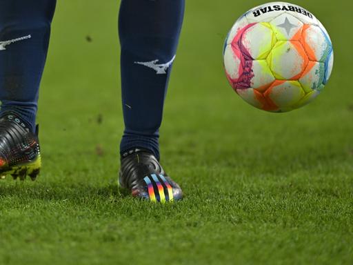 Szene aus dem Fußball-Bundesligaspiel FC Augsburg - VfL Bochum mit Regenbogenfarben auf dem Schuh eines Bochumer Spieler und auf dem Spielball

