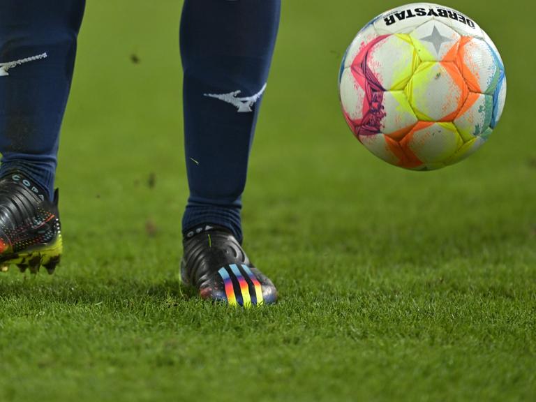 Szene aus dem Fußball-Bundesligaspiel FC Augsburg - VfL Bochum mit Regenbogenfarben auf dem Schuh eines Bochumer Spieler und auf dem Spielball

