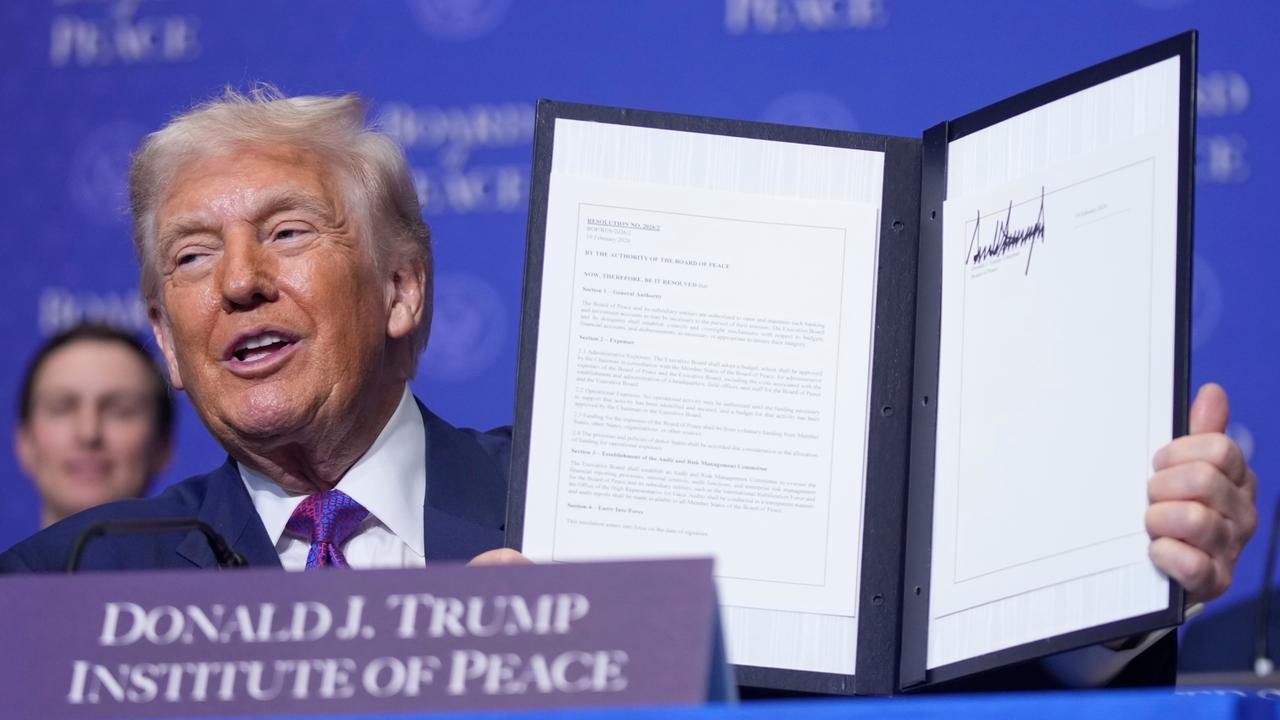 Donald Trump präsentiert eine unterzeichnete Urkunde. Die Platzkarte vor ihm trägt die Aufschrift "Donald J. Trump - Institute of Peace".