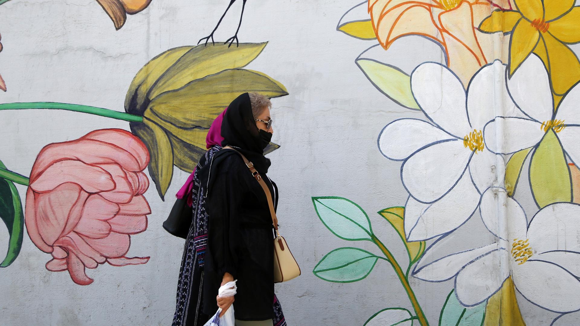 Eine Frau mit Kopftuch läuft an einem Wandbild mit Blumen und Vogel in einer Straße in Teheran vorbei.