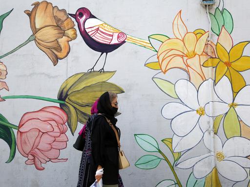 Eine Frau mit Kopftuch läuft an einem Wandbild mit Blumen und Vogel in einer Straße in Teheran vorbei.