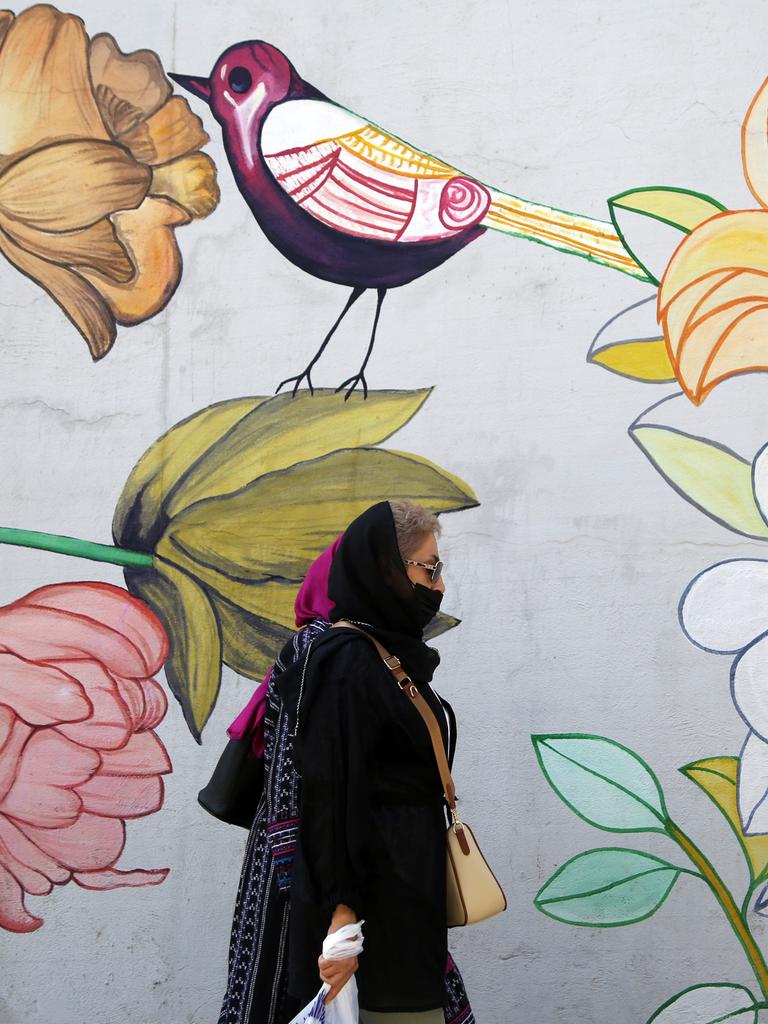 Eine Frau mit Kopftuch läuft an einem Wandbild mit Blumen und Vogel in einer Straße in Teheran vorbei.