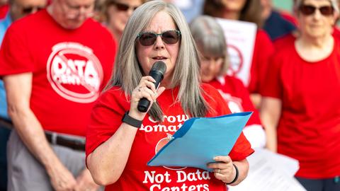Holly Manke hält im Juli 2026 in Virginia (USA) während einer Kundgebung gegen Rechenzentren eine Rede. Sie trägt ein rotes Tshirt mit der Aufschrift "Grow Tomatos, not Data Centers". Hinter ihr stehen weitere Protestierende. Holly Manke hält im Juli 2026 in Virginia (USA) während einer Kundgebung gegen Rechenzentren eine Rede. Sie trägt ein rotes Tshirt mit der Aufschrift "Grow Tomatos, not Data Centers". Hinter ihr stehen weitere Protestierende.