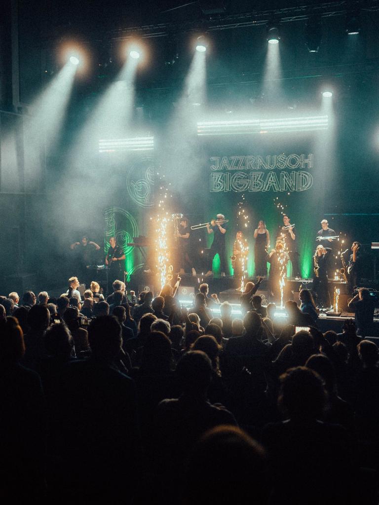 Ein dunkler Konzertsaal, auf der hell beleuchteten Bühne spielt die Jazzrausch Bigband zwischen Lichtfontänen. 