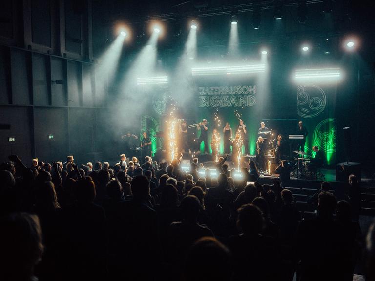 Ein dunkler Konzertsaal, auf der hell beleuchteten Bühne spielt die Jazzrausch Bigband zwischen Lichtfontänen. 