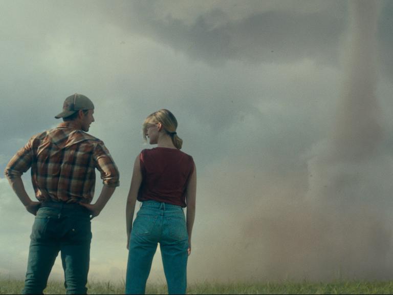 Filmszene aus Twisters zeigt Glen Powell, links, und Daisy Edgar-Jones in der Rückenansicht, wie sie auf einen Tornado schauen.