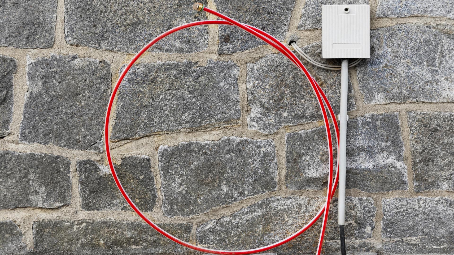 Das Foto zeigt einenTelekom- Hausanschluss mit Glasfaserkabel: Ein gerolltes Kabel lehnt an einer Mauer, daneben ein Verteilerkasten.